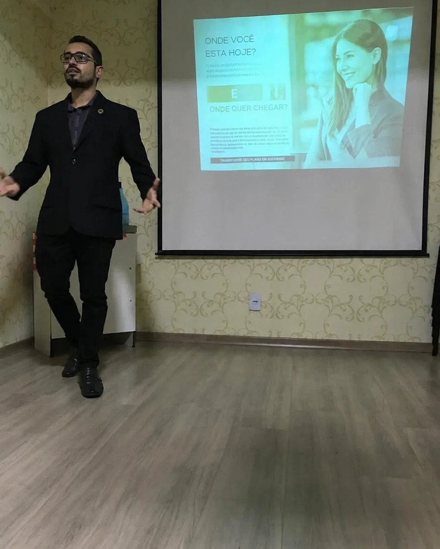Alex apresentando para um grupo, ao lado de uma tela de projeção